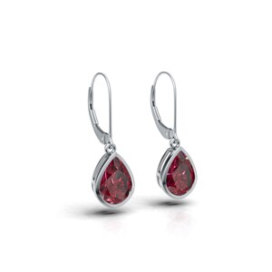 May include: A pair of silver drop earrings. Each earring has a pear-shaped, deep red gemstone set in a silver frame. The earrings have a lever-back closure. The background is white.