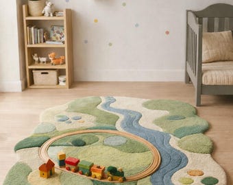 May include: A whimsical, landscape-shaped rug with a river design in shades of green and blue. A wooden train set with colorful cars and a small house sits on a circular track. The rug is on a wooden floor.
