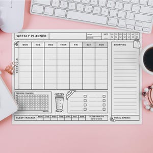 以下が含まれることがあります： スケジュール、運動追跡、睡眠モニタリング用のグリッドレイアウトを備えた白い週間プランナー。コーヒーカウントセクションとショッピングリストエリアが含まれています。キーボード、マウス、コーヒーカップがピンク色の表面にあります。