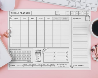 May include: A white weekly planner with a grid layout for scheduling, exercise tracking, and sleep monitoring. Features a coffee count section and a shopping list area. Includes a keyboard, mouse, and a cup of coffee on a pink surface.