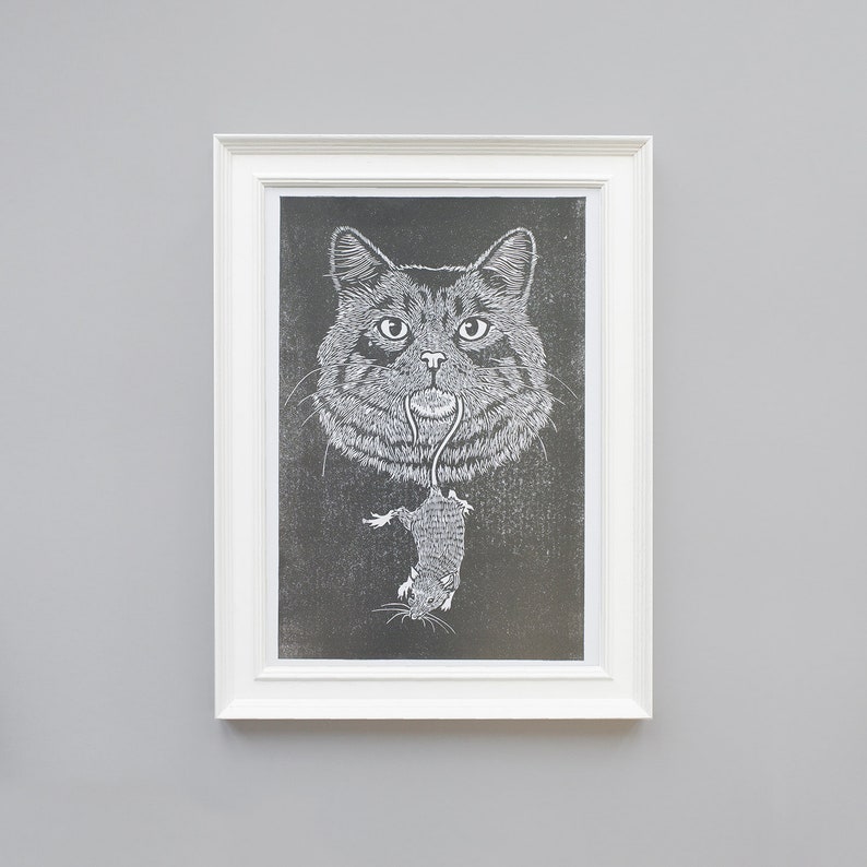 Cat with mouse. Hand printed lino print. A4 size. Grey and white. Shown in white picture frame on grey background.  Made in the UK by the Type Stack Studio