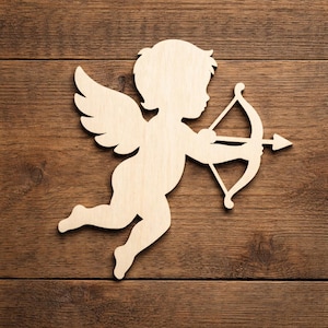 Puede incluir: Silueta de madera de Cupido, una figura alada con arco y flecha. Cupido está representado en vuelo, con las alas extendidas y una flecha apuntando hacia adelante. El recorte es de madera clara, sobre un fondo de madera marrón.