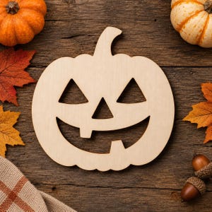May include: A flat, light-coloured wooden cutout in the shape of a jack-o'-lantern with triangular eyes and a nose, and a wide, toothy grin. The pumpkin shape is centred, featuring a smooth surface and a distinct stem at the top centre.