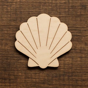 Może przedstawiać: Drewniany wycięty kształt muszli z wytrawionymi liniami, spoczywający na ciemnej drewnianej powierzchni. Jasne drewno kontrastuje z ciemnym tłem, podkreślając kształt i szczegóły muszli. Idealny do dekoracji w stylu plażowym lub projektów DIY.