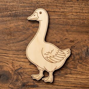 Könnte beinhalten: Ein Holzausschnitt einer Gans mit eingravierten Details. Die Gans hat einen langen Hals, einen Schnabel und ein detailliertes Flügeldesign. Der Ausschnitt besteht aus hellem Holz und liegt auf einer Holzoberfläche.