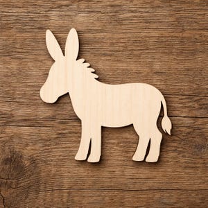 May include: A flat, light-colored wooden cutout in the shape of a donkey, featuring a smooth surface with visible natural wood grain patterns, long ears, a short mane, and a tail, presented in a side profile view with clean, laser-cut edges.