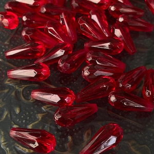 Puede incluir: Un conjunto de cuentas facetadas en forma de lágrima, de un tono rojo vibrante. Las cuentas están hechas de un material transparente, que atrapa la luz y muestra sus cortes geométricos. Ideales para la creación de joyas.