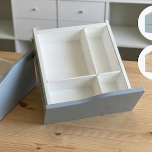 May include: A light gray and white wooden drawer with interior compartments, ideal for organizing small items. The drawer is open, revealing the white interior. Two smaller drawer examples are shown in the upper right corner.