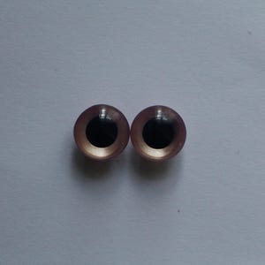 May include: A pair of craft eyes, each with a light brown iris and a black pupil. The eyes have a glossy finish and are set against a plain, light background. Suitable for doll making or other craft projects, these eyes add a realistic touch.