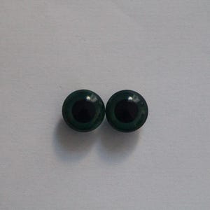 Op de afbeelding: Twee donkergroene, ronde knutselogen met zwarte pupillen. Deze plastic ogen zijn ontworpen voor gebruik in diverse knutselprojecten, zoals knuffels of poppen. De ogen zijn geplaatst tegen een effen witte achtergrond.