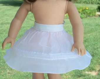May include: A white tulle petticoat with a white satin waistband. The petticoat is worn by a doll with brown hair and brown eyes. The doll is wearing a white headband.