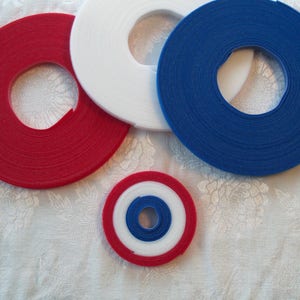 May include: Four rolls of hook and loop tape in red, white, and blue. The rolls are arranged in a circle with the smallest roll in the center.