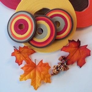 May include: Assortment of colorful fabric rolls with a fall theme. The rolls are in shades of red, orange, yellow, brown, and green. There are also two small maple leaves and a sprig of berries.