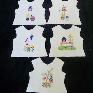 May include: Five white fabric pieces with embroidered designs. Each features a different birdhouse scene with flowers, birds, and patriotic elements. The designs include red, white, blue, yellow, and green colors.