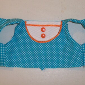 May include: A turquoise blue vest with white polka dots and a white collar with orange trim. The vest has two white buttons with orange centers.