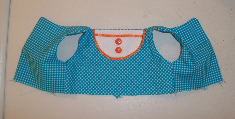 May include: A turquoise blue vest with white polka dots and a white collar with orange trim. The vest has two white buttons with orange centers.