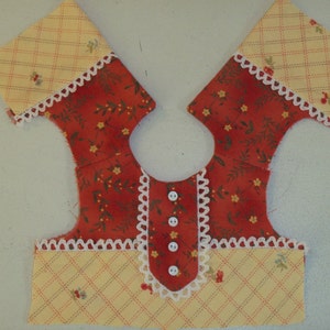 May include: A red and yellow fabric doll dress with white lace trim and buttons down the front.