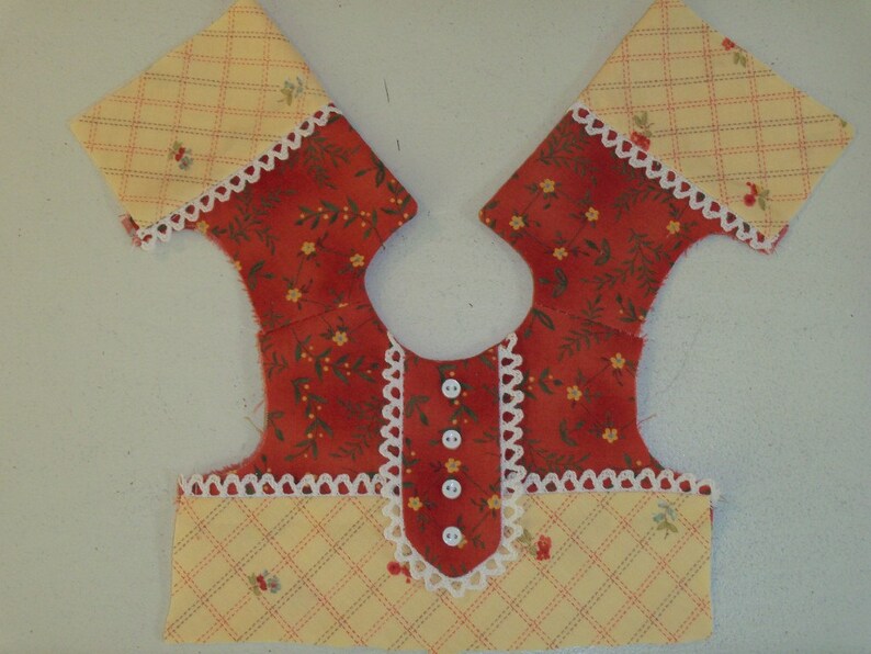 May include: A red and yellow fabric doll dress with white lace trim and buttons down the front.