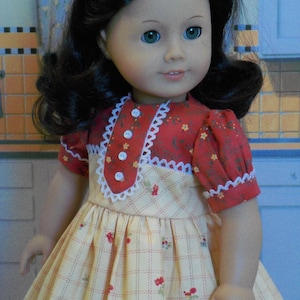 May include: A doll wearing a yellow and red dress with a white lace trim. The dress has a plaid pattern and small red flowers. The doll has long dark hair and blue eyes.