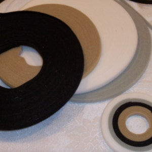 May include: Close-up of a variety of hook and loop tape rolls in different colors, including black, beige, white, and gray. The rolls are arranged in a circle, with the black roll in the center.