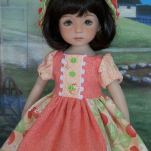 May include: A doll wearing a pink and green dress with a strawberry print and a matching green and white hat. The doll has brown hair and blue eyes.