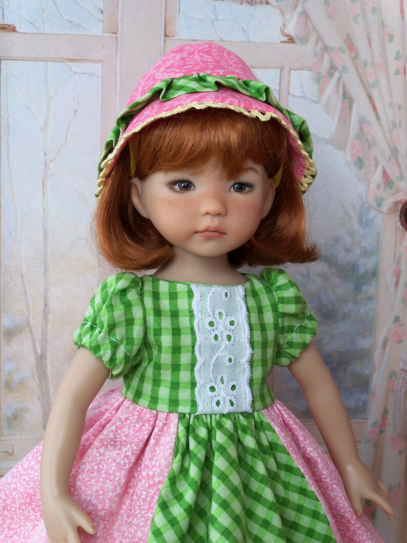 May include: A doll wearing a green and pink gingham dress with a white lace trim and a pink and green hat. The doll has red hair and blue eyes.