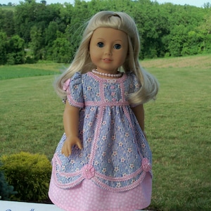 May include: A doll wearing a blue and pink floral dress with a pearl necklace and white shoes. The dress has pink trim and a pink polka dot skirt. The text on the image says "Farmcookies Designs Sewing Pattern for 18" Dolls" and "Fairy Slipper".