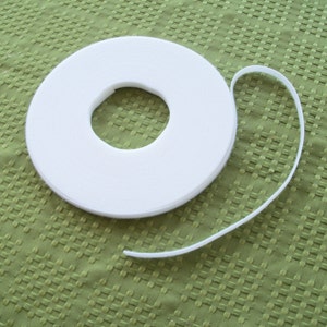 May include: A roll of white double-sided adhesive tape on a green textured surface.