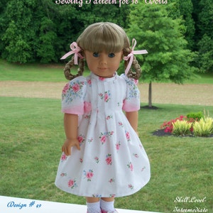 May include: A white dress with a floral print and pink accents for an 18-inch doll. The dress has a gathered skirt and puffed sleeves. The doll is wearing white socks and pink shoes. The dress is called "Butterfly Kisses" and is design #49.