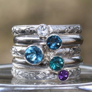 Set of 5 rings stacked together. Top and bottom bands hold small 3mm round gems on band E. The 2 bands beside the outer bands hold a 4mm round gem on band B. The middle ring holds a 5mm round gem on band E.