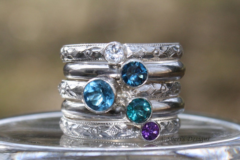 Set of 5 rings stacked together. Top and bottom bands hold small 3mm round gems on band E. The 2 bands beside the outer bands hold a 4mm round gem on band B. The middle ring holds a 5mm round gem on band E.