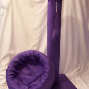 May include: Purple cat bed with a round, cushioned bed and a tall, cylindrical scratching post. The post has a purple flower on top.