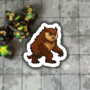 May include: A sticker depicting a cartoon owl-like creature with brown and tan fur, a stern expression, and sharp claws. The sticker is on a grey surface, with several dice visible in the background.
