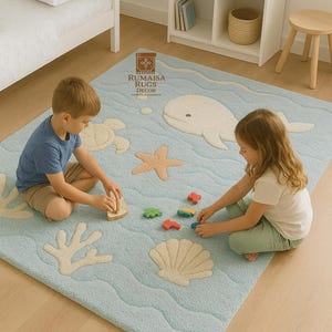 Puede incluir: Alfombra infantil azul claro con temática oceánica, con diseños de ballena, estrella de mar y conchas. La alfombra tiene un patrón ondulado y está hecha a mano. Los niños juegan en la alfombra con coches de juguete y un juguete de madera.