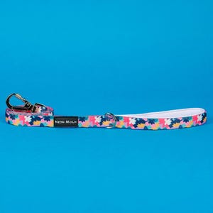 May include: A patterned dog lead featuring a floral design in pink, yellow, blue, and green. It has a silver metal clasp and a white padded handle. The text "Neon Moon" is printed on the lead.