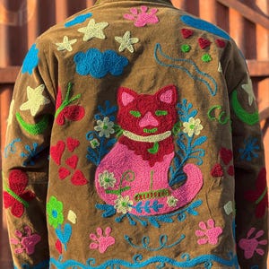 May include: A white ceramic mug with a black handle and the text "But First, Coffee" in a bold, black font. The mug is set against a blurred background, suggesting a cozy setting.