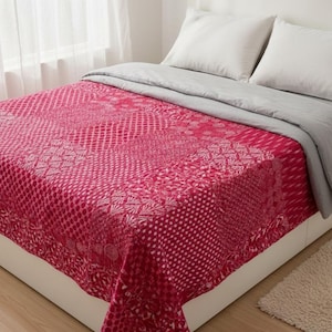 Może przedstawiać: Łóżko z różową, wzorzystą kołdrą i szarą narzutą. Kołdra ma różne wzory, w tym kropki i motywy kwiatowe. Na łóżku leżą białe poduszki. Na podłodze widoczny jest mały dywanik.