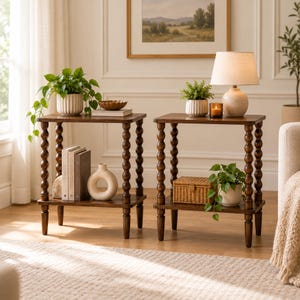 May include: Two matching dark brown wooden side tables, each featuring four legs with a stacked ball design and a lower shelf. The tables are square-topped and hold various decorative items including potted plants, books, a lamp, and a basket.