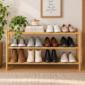 May include: A three-tier bamboo shoe rack holding various footwear including white sneakers, loafers, boots, and slip-ons. The top shelf features a stack of three books titled The Kinfolk Home, At Home, and Live Beautifully, plus a candle.