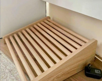 May include: A wooden drying rack with multiple parallel dowels. The rack is made of light-colored wood and is angled, with a rectangular frame. The rack is designed for drying items. A black power adapter is next to the rack.