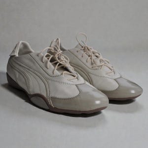 May include: Off-white Puma trainers with matching laces. The shoes feature a leather upper with stitched details and a brown sole. The design includes the Puma logo on the side.