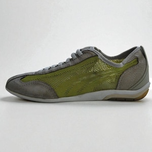 May include: A gray and green athletic shoe. The shoe features a mesh upper in a vibrant green, complemented by gray suede overlays on the toe, heel, and lace area. The sole is a light gray with a brown accent at the heel.