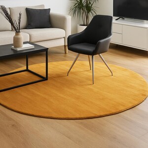 May include: A modern living room featuring a mustard yellow round rug, a black chair with silver legs, and a black coffee table. A beige sofa with a black pillow and a framed abstract art piece complete the scene.