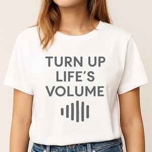 May include: White t-shirt featuring the grey text "TURN UP LIFE'S VOLUME" and a sound wave graphic. The t-shirt has a crew neck design.