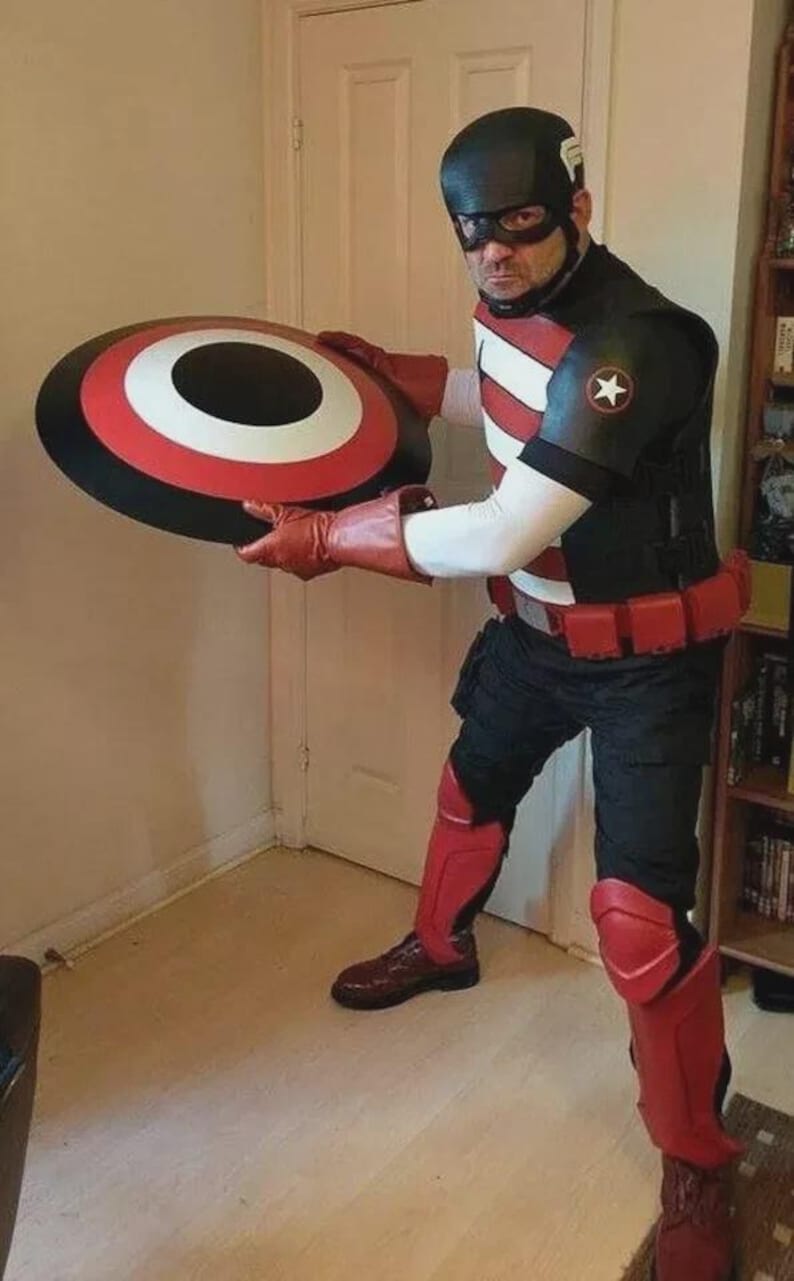 Puede incluir: Un disfraz negro y rojo con un escudo con un dise&ntilde;o blanco, rojo y negro. El atuendo incluye un casco, guantes y botas negros. El disfraz tiene un emblema de estrella en el hombro.