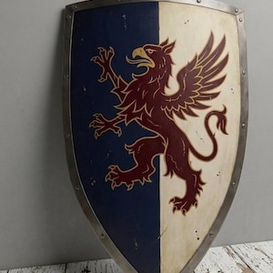 Peut inclure: Un bouclier de type écu avec un design divisé verticalement, bleu foncé à gauche et crème à droite. Un griffon marron est peint au centre. Le bouclier possède une bordure en métal argenté fixée par des rivets visibles sur tout le pourtour.