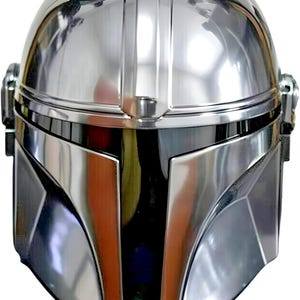 Op de afbeelding: Een glanzende, zilveren helm met een opvallend ontwerp. De helm heeft een afgeronde bovenkant, een centrale verticale richel en hoekige gelaatstrekken. Het reflecterende oppervlak cre&euml;ert highlights en schaduwen, waardoor de metalen uitstraling wordt benadrukt. Het ontwerp van de helm doet denken aan een ruimtethema.