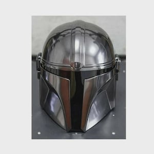 Op de afbeelding: Een glanzende, zilverkleurige Mandalorian helm met een opvallend T-vormig vizier. De helm heeft een afgeronde bovenkant met verticale groeven en een gladde, metalen afwerking. Het ontwerp doet denken aan sciencefiction.