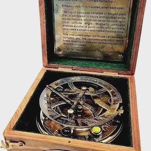 Op de afbeelding: Een vintage messing kompas en zonnewijzer instrument, gehuisvest in een houten kist. Het kompas heeft ingewikkelde details en is gemarkeerd met "GILBERT & SONS London". De kist bevat een messing plaat met beschrijvende tekst.