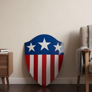 Könnte beinhalten: Ein Schild mit patriotischem Design, mit einem blauen Oberteil mit drei weißen Sternen und rot-weißen Streifen darunter. Das Schild lehnt an einer Wand und zeigt ein klassisches Thema.